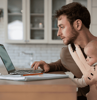 Father working on laptop with baby in carrier at home, digital health concept.